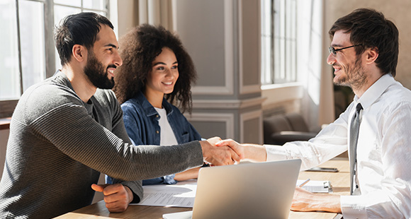 three people smiling and shaking hands at a business meeting demonstrating collaboration and partnership in a bright office environment