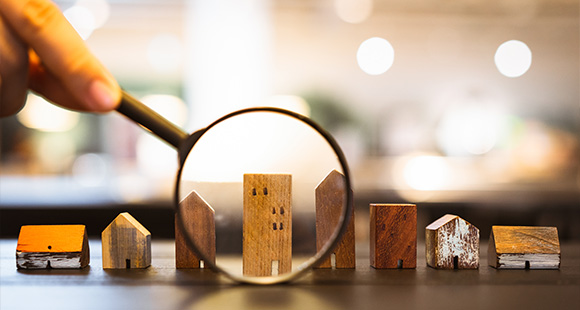 hand holding a magnifying glass over miniature wooden houses emphasizing details and showcasing seven unique designs